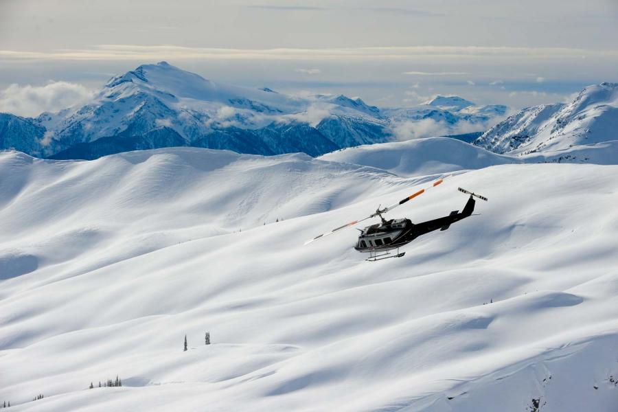 Helikopter über schneededeckten Bergen von Selkirk Tangiers Heliskiing